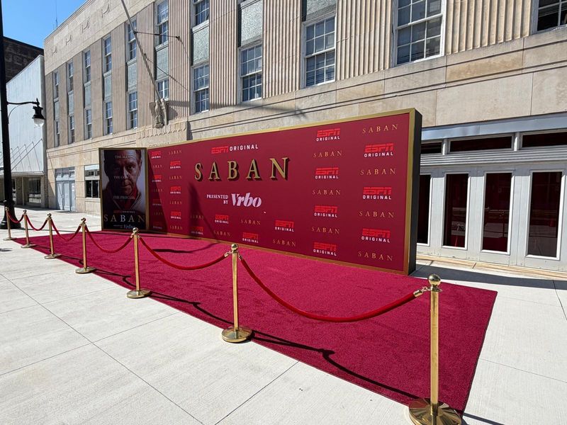 Gold-framed red step-and-repeat banner wall printed with ESPN Original and Saban logos, with a red carpet and brass stanchions in front