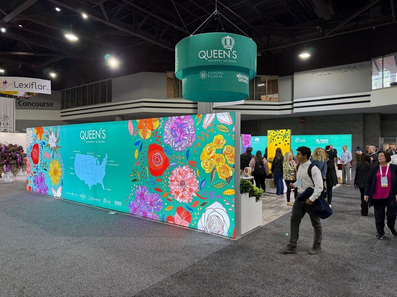 Queen's Bouquet Network trade show booth with a floral-pattern backlit wall and hanging circular sign